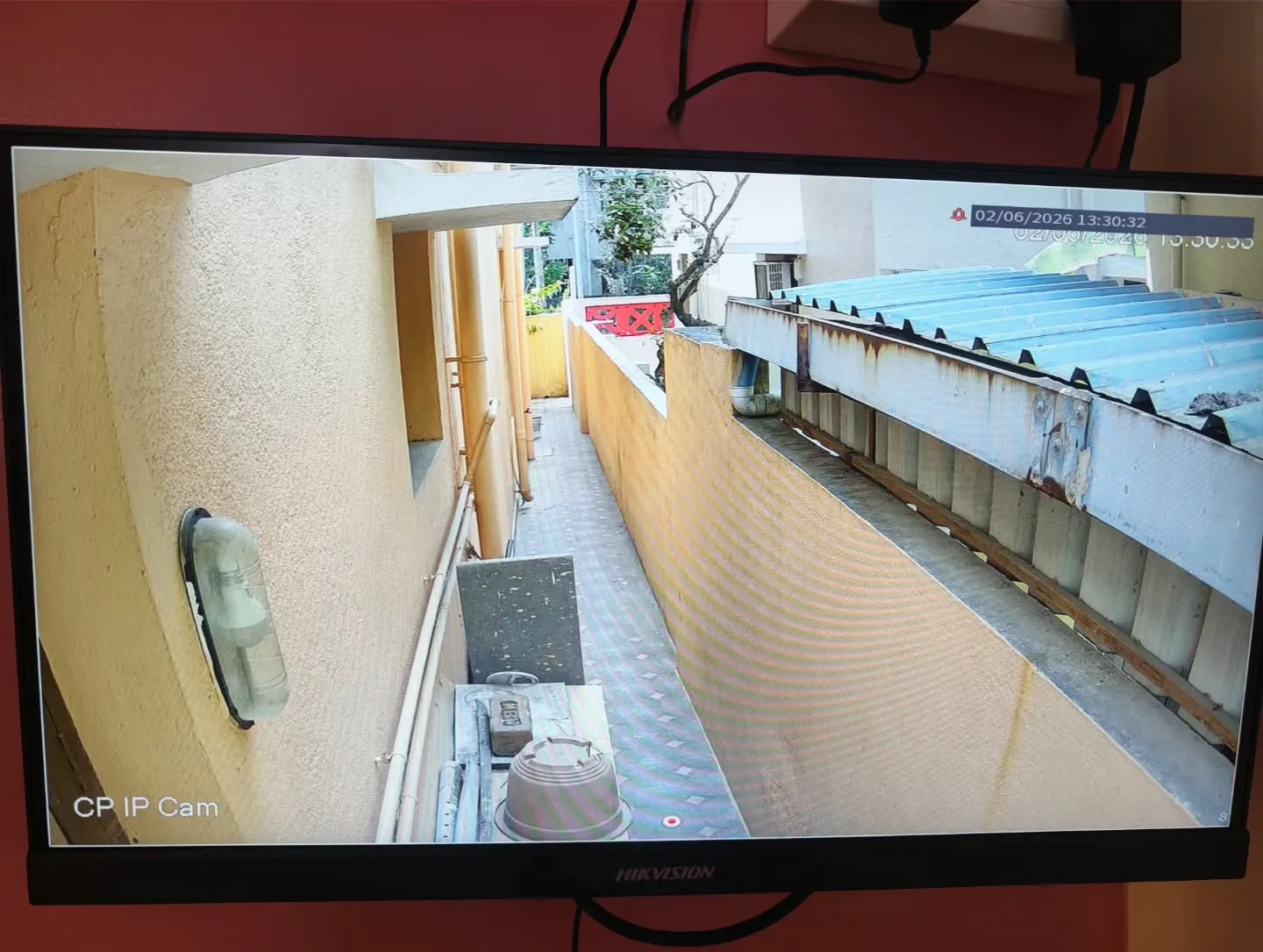 Narrow outdoor view from a CP Plus 4MP STQC IP camera installation monitoring a long residential compound pathway and adjacent building boundaries.