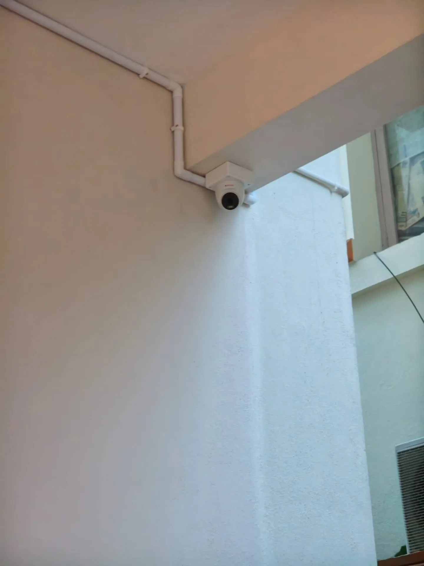 ​A compact white CP Plus dome camera mounted under a structural ceiling beam with neat rigid PVC conduit piping.