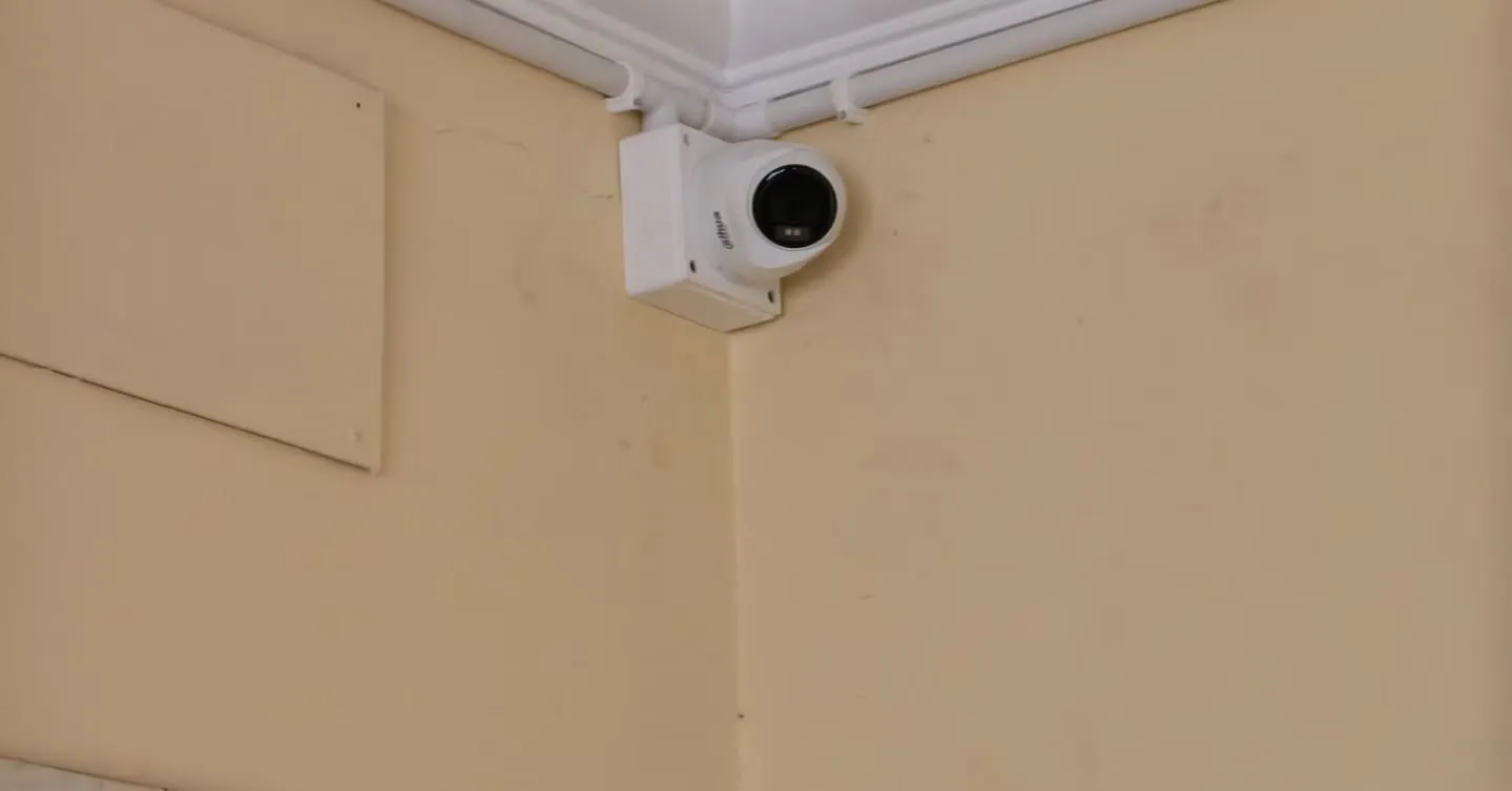 Close-up view of a professional Dahua dome CCTV camera neatly installed in a room corner on a white junction box, featuring clean wiring routed through white PVC conduit pipes running along the ceiling molding line.