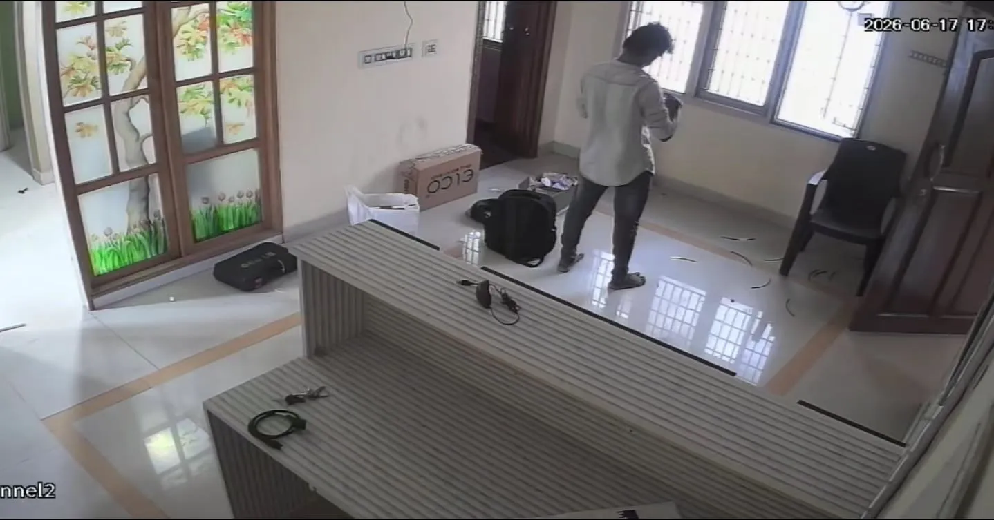 High-angle wide indoor security camera view from a Dahua 2MP Dual Light camera capturing Channel 2 coverage of a commercial office reception area in Velachery, showing a technician standing near a long wooden desk setup with installation tools, a backpack, and equipment boxes on the floor.