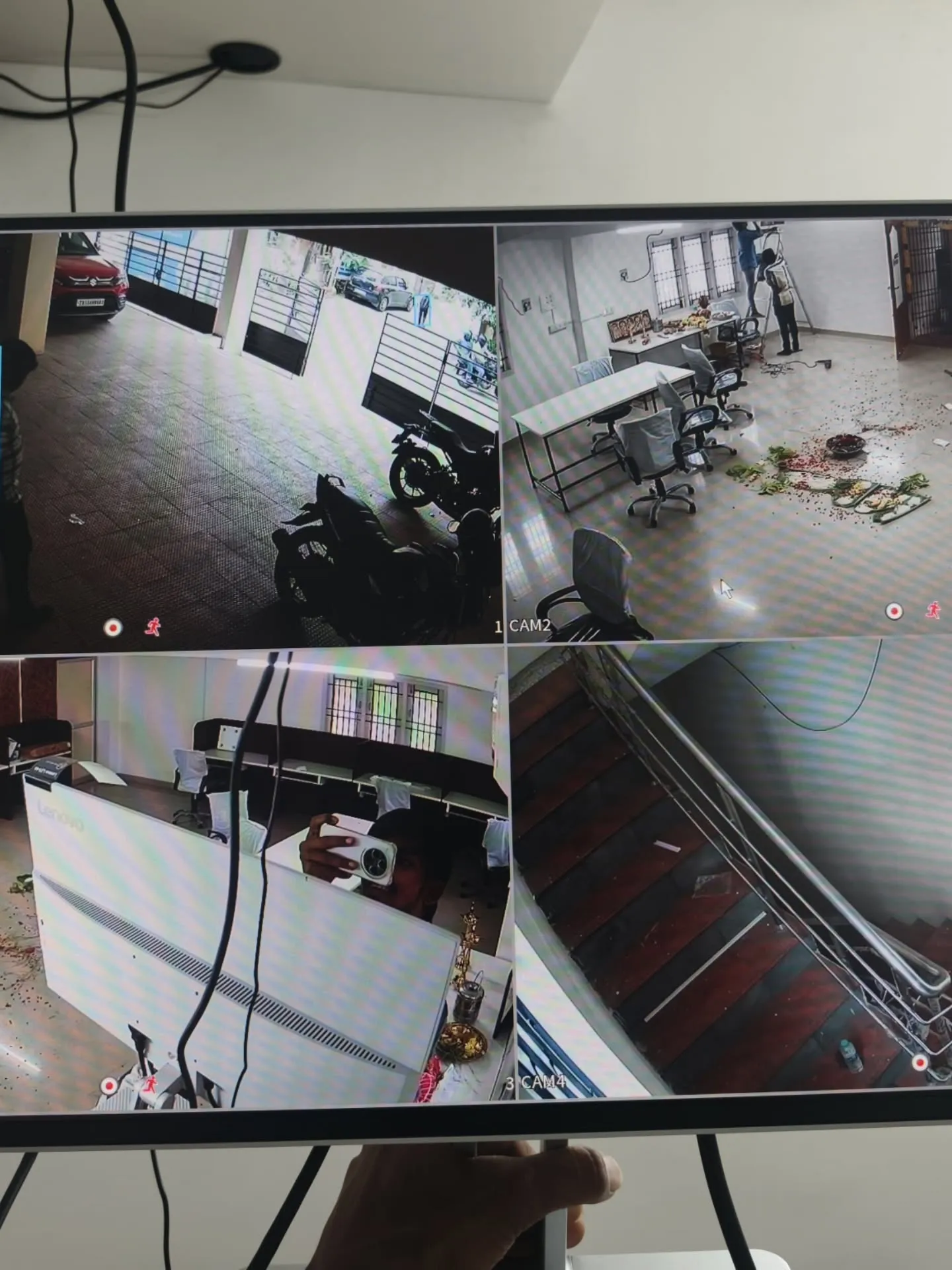 ​A monitor showing a 4-channel live matrix grid from CP Plus 5MP cameras monitoring office interiors, entrance stairs, and parking facilities.