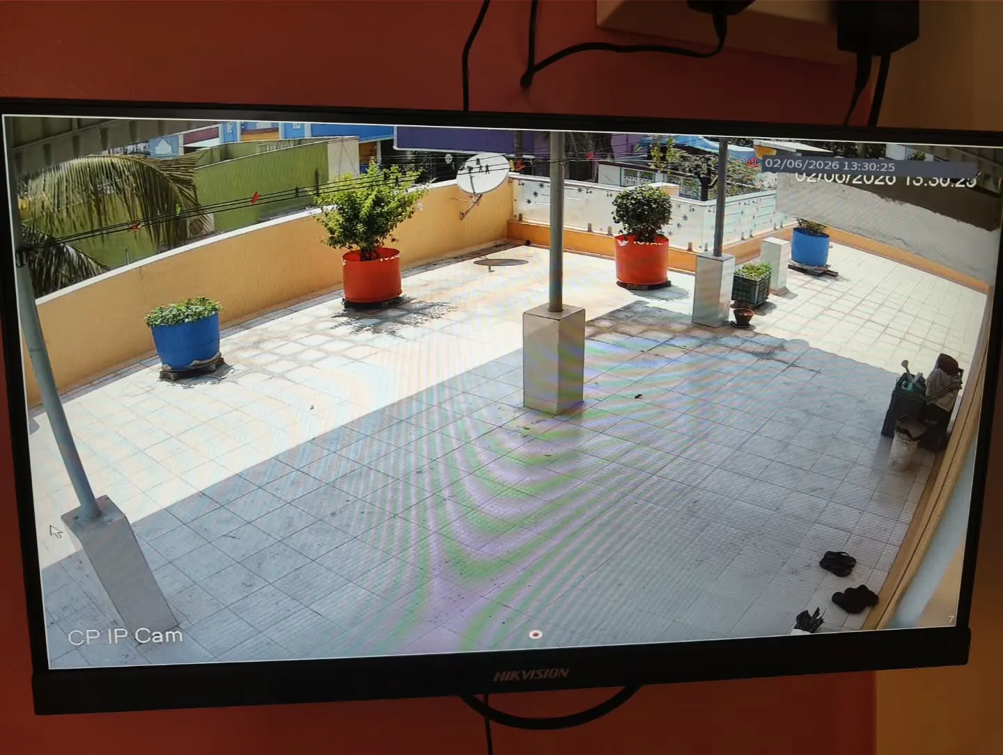 CP Plus 4MP STQC IP camera installation view monitoring an open residential terrace area with potted plants and tiled flooring.