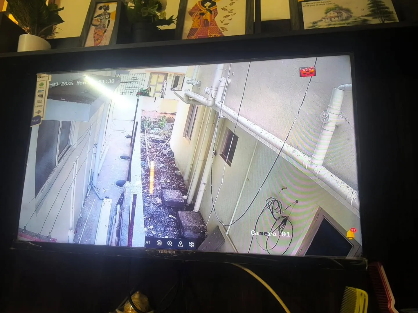Outdoor Hikvision security camera view covering narrow residential side corridor and drainage pipeline perimeter