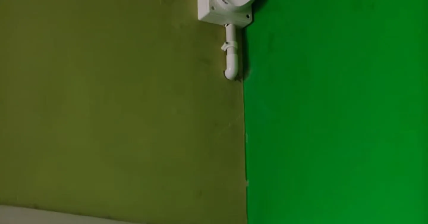 Indoor Dahua dome CCTV camera neatly corner-mounted on a white surface junction box on a olive-green wall adjacent to a bright green wall surface, with protected video cables dropping directly down through a rigid PVC conduit bend.