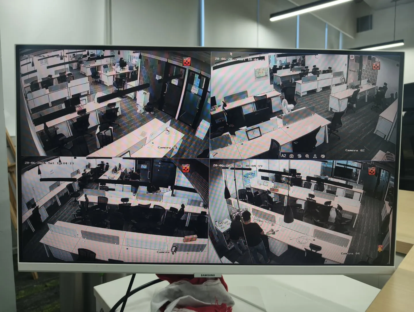 A monitor screen displaying a 4-channel matrix feed from Hikvision 5MP dome cameras covering corporate workbenches and desks at SquareShift Technologies.