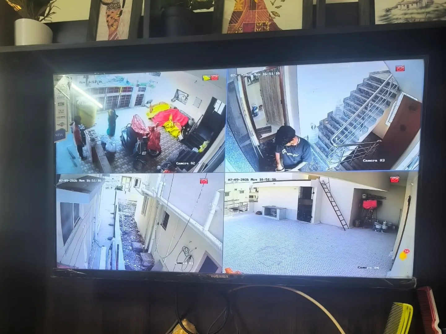Residential living room TV displaying live 4 camera Hikvision CCTV footage with DVR setup on wooden console table in Keelkattalai
