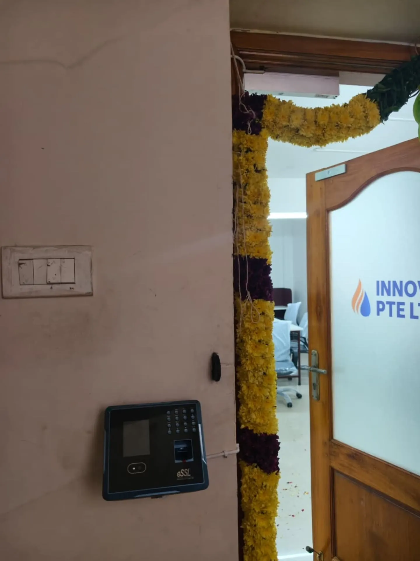 ​A wall-mounted eSSL MB160 facial and fingerprint biometric attendance terminal installed at an office entrance door for keyless security.