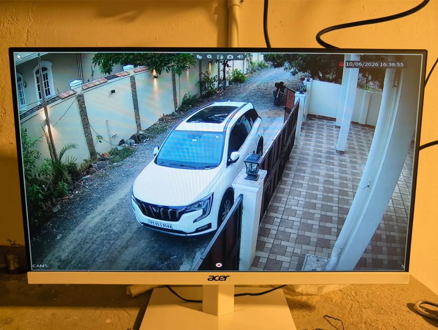 ​A detailed full-screen camera channel on a monitor screen tracking a white Mahindra XUV700 parked in an apartment driveway path.
