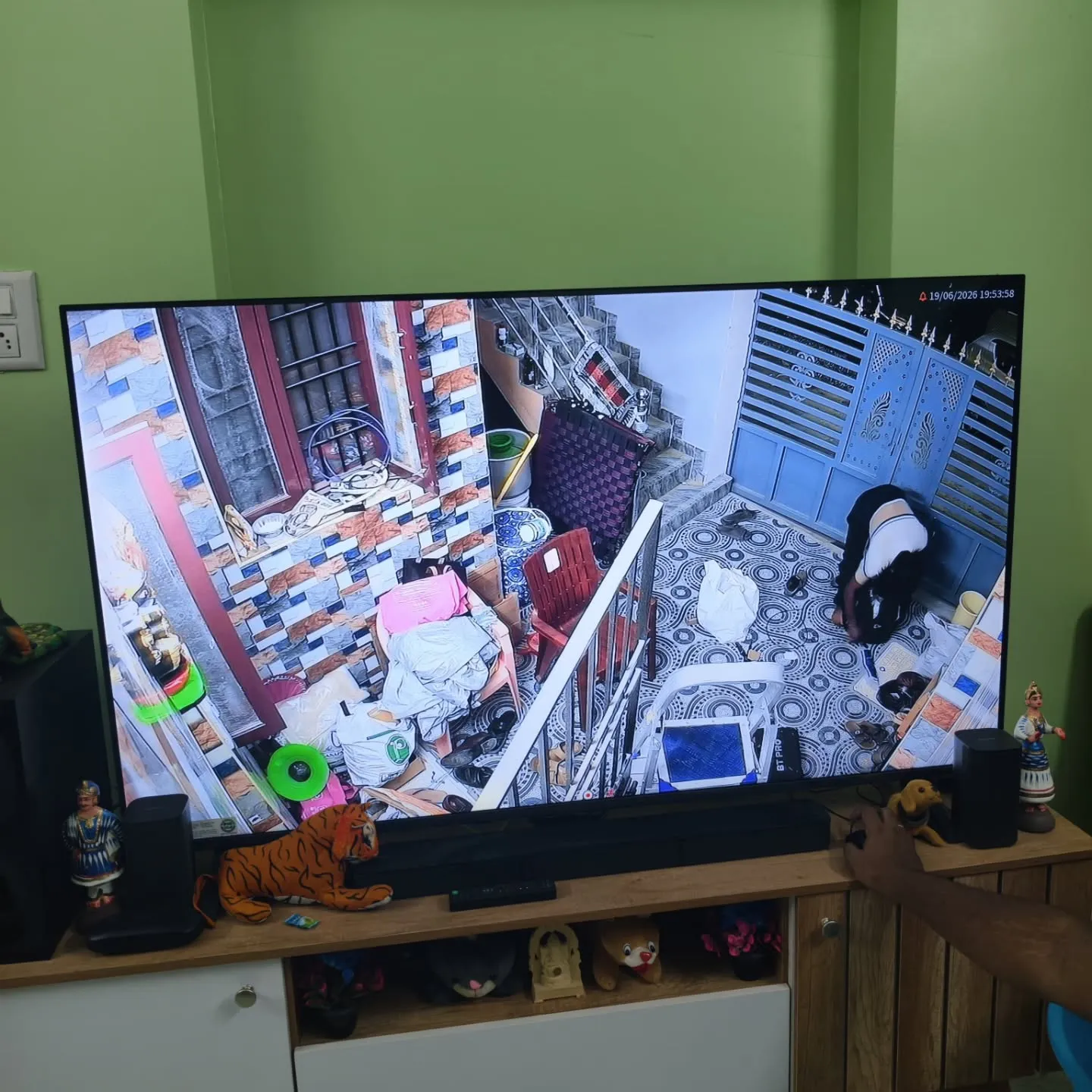 An elevated corner angle displayed full-screen on a television, showcasing a Cpplus 2MP HD Dual Light camera monitoring a residential compound veranda, main entrance gate, and staircase area.