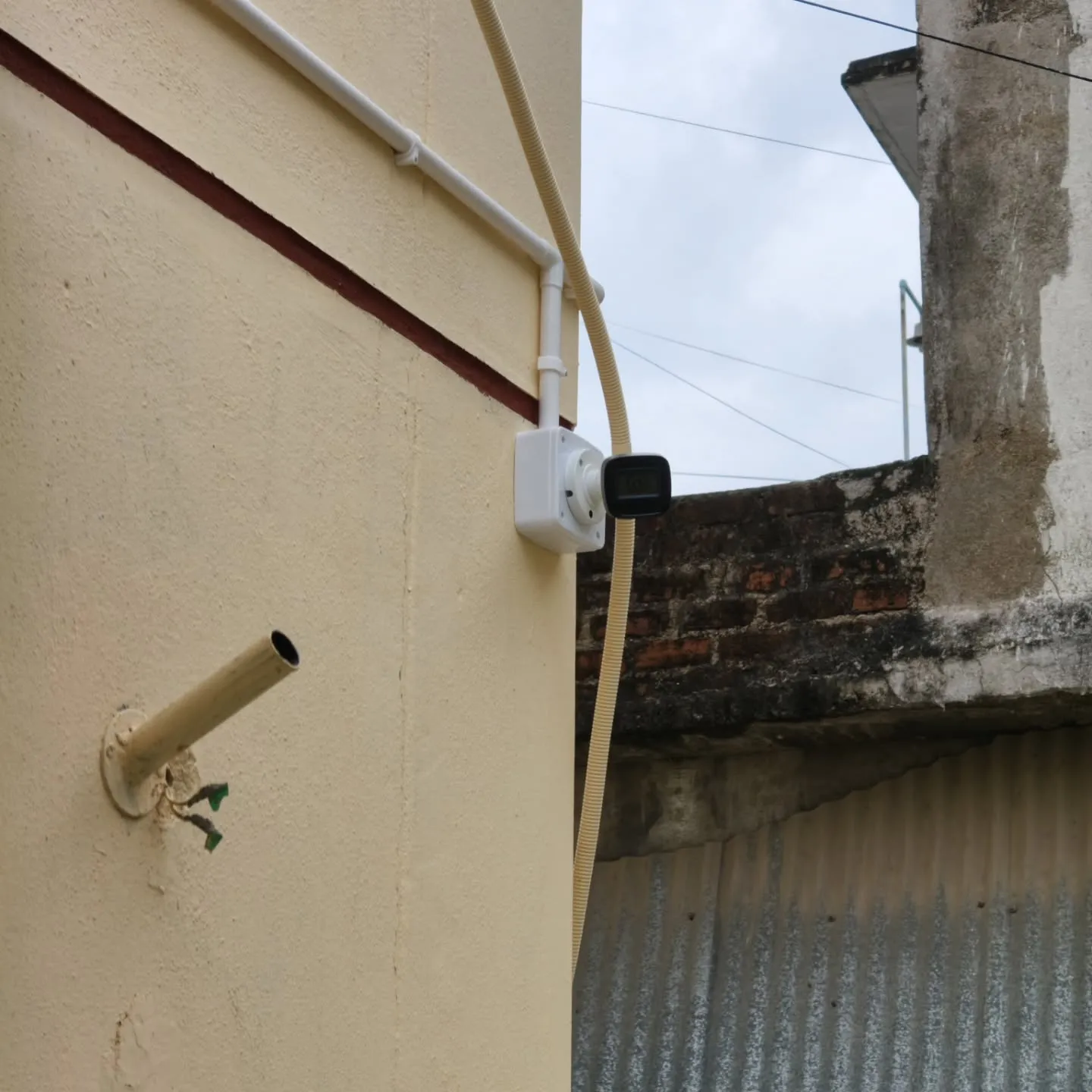 A wall-mounted Hikvision bullet camera connected with neat rigid PVC pipe routing and an outdoor junction box on a residential wall.