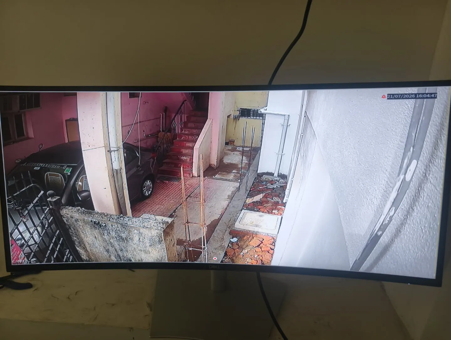 A clear screen display showing a CP Plus outdoor camera feed capturing the driveway, parking zone, and exterior staircase of a residential building.