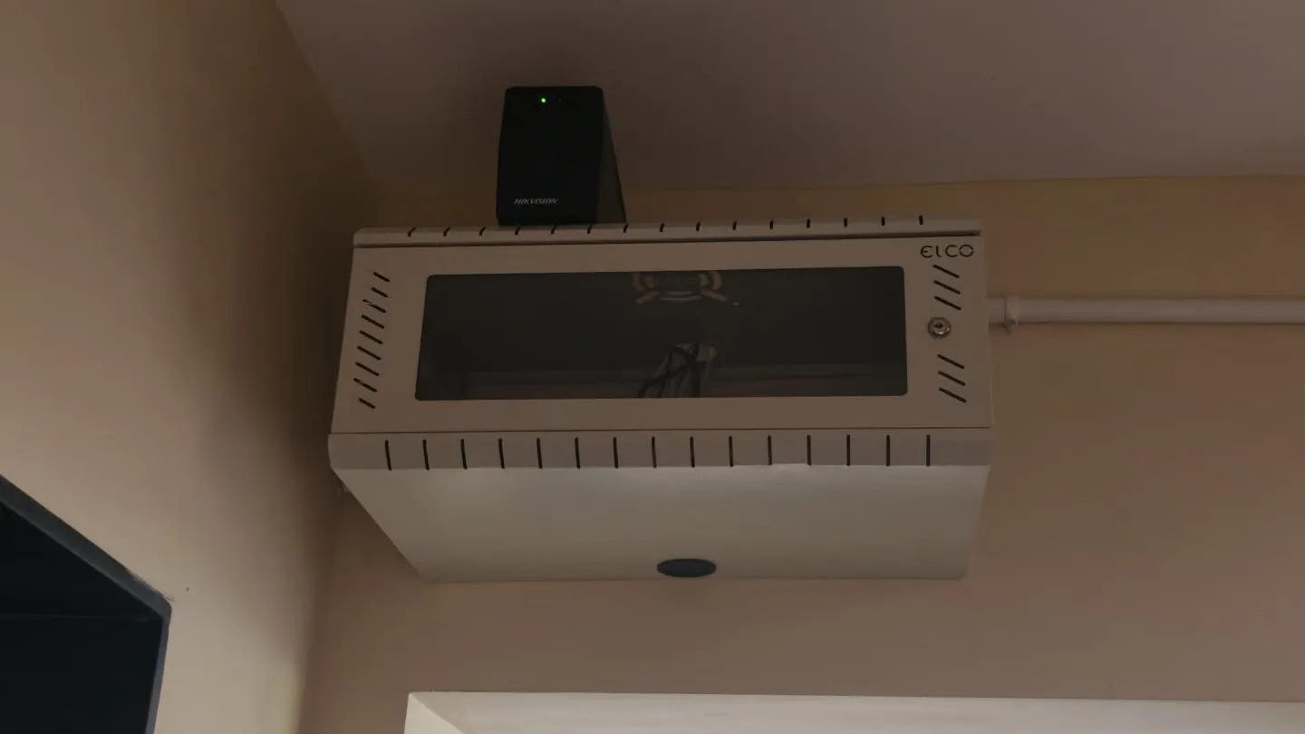 ​A wall-mounted white network rack enclosure housing the Superlive Plus NVR with a Hikvision 1KVA UPS positioned securely on top