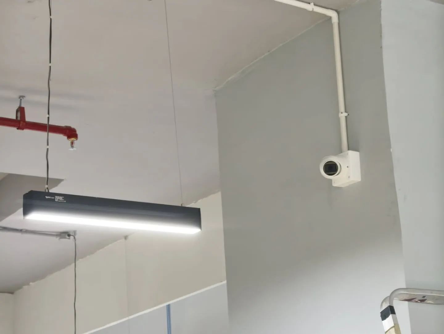 A sleek white Hikvision dome camera cleanly mounted on a concrete pillar with neat PVC conduit wiring running along the ceiling line.