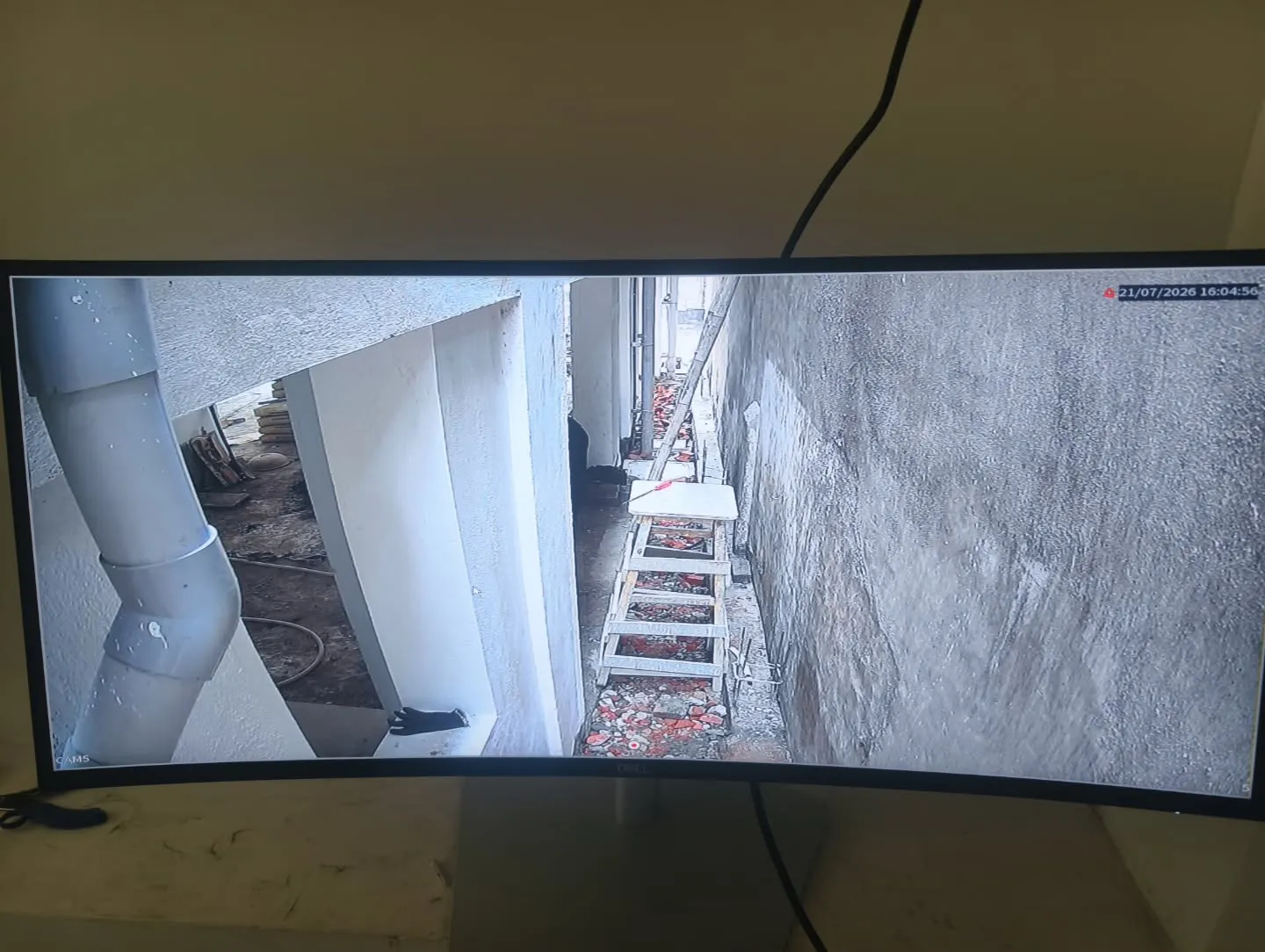 A high-definition view from a CP Plus camera mounted on an extension stand monitoring a narrow side pathway and drainage pipe layout.