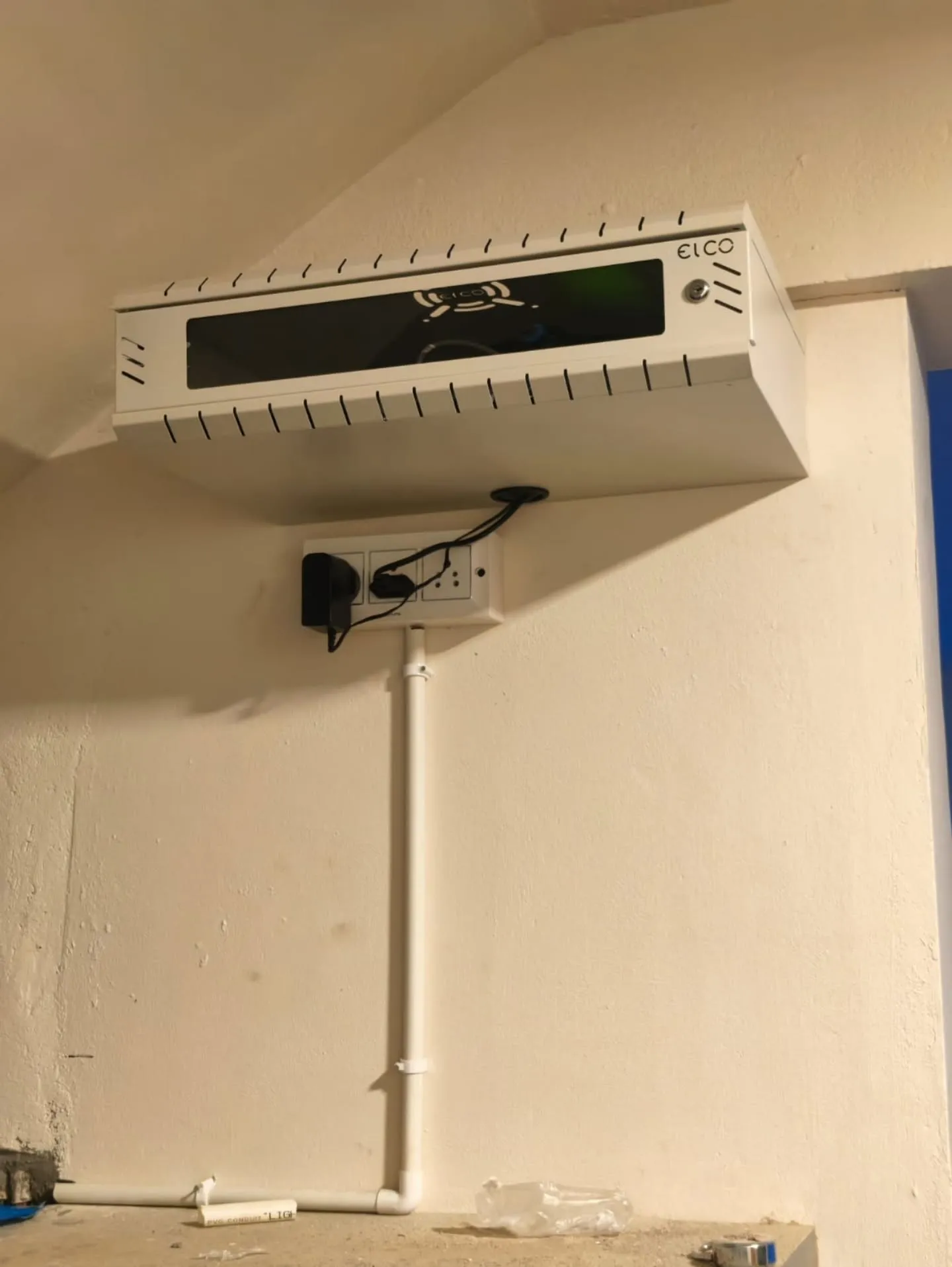A clean, wall-mounted white Elco 2U network server rack housing security components cleanly above a power outlet socket.