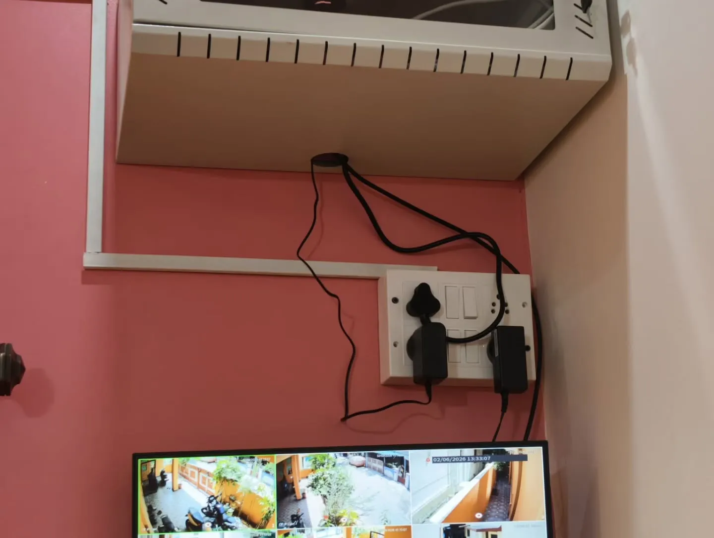 Wall-mounted CCTV network rack installation with neat PVC casing layout, power adapter connections, and a multi-channel security monitor display below.