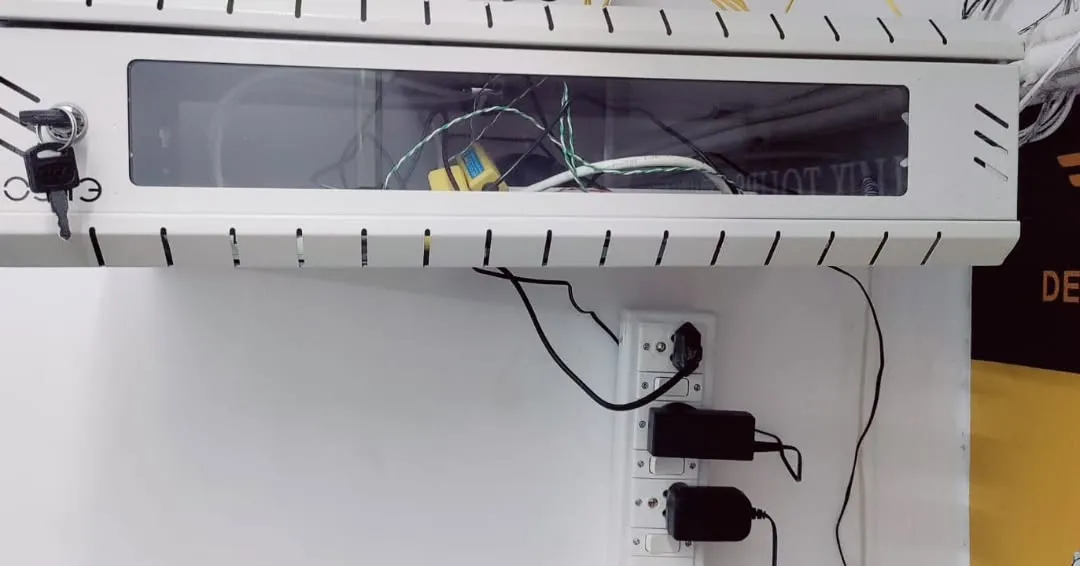 A white wall-mounted network enclosure rack securely housing centralized security system hardware above a vertical power strip.